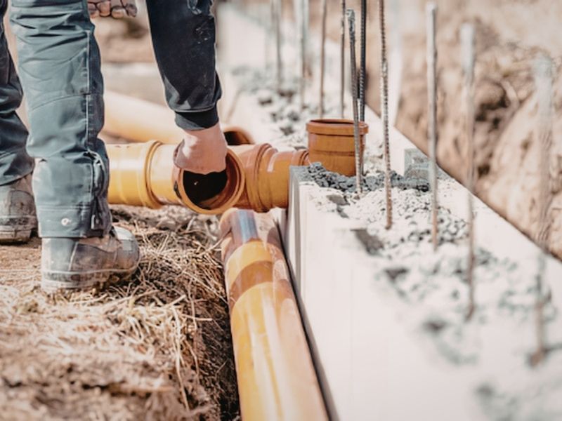 Construction worker installing underground stormwater drainage pipes beside a building foundation for site drainage management