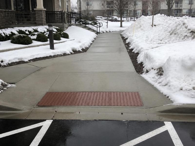 Barrier-free winter walkway in Grand Rapids with a curb ramp, tactile surface, gentle slope, and cleared snow along both sides.